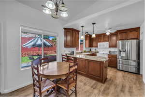 Kitchen featuring white appliances, a peninsula, light wood-style floors, light stone countertops, and a chandelier