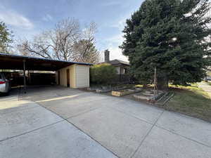 Garage featuring concrete driveway, a vegetable garden, and a carport