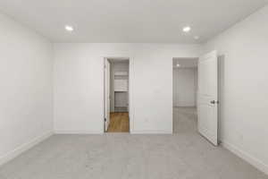 Unfurnished bedroom featuring light carpet, a walk in closet, and recessed lighting