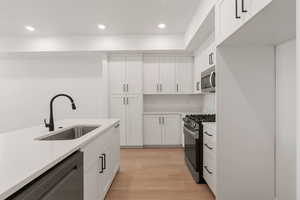 Kitchen with appliances with stainless steel finishes, white cabinetry, light wood-style flooring, recessed lighting, and light stone counters