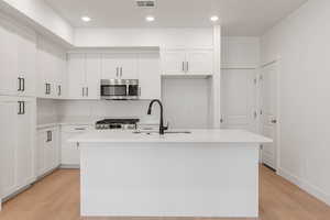 Kitchen featuring stainless steel appliances, white cabinetry, light wood-style floors, light stone countertops, and recessed lighting