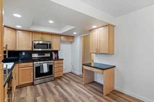 Kitchen featuring appliances with stainless steel finishes, light wood finished floors, decorative backsplash, a raised ceiling, and recessed lighting