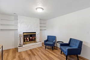 Sitting room with a stone fireplace, a textured ceiling, and wood finished floors