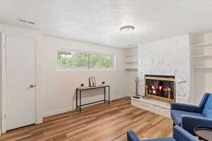 Sitting room with a stone fireplace, a textured ceiling, and wood finished floors