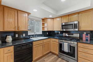 Kitchen featuring appliances with stainless steel finishes, light wood finished floors, decorative backsplash, a raised ceiling, and recessed lighting