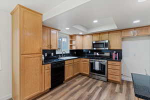 Kitchen featuring appliances with stainless steel finishes, light wood finished floors, decorative backsplash, a raised ceiling, and recessed lighting