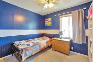 Carpeted bedroom with a ceiling fan and a wainscoted wall