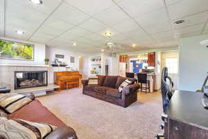 Living area with light colored carpet, a fireplace, a ceiling fan, a desk, and a chandelier