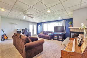 Carpeted living room with a drop ceiling, a glass covered fireplace, french doors, ceiling fan, and a desk