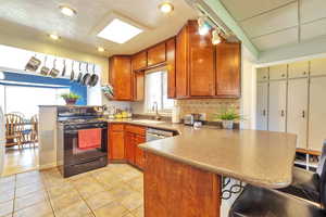 Kitchen featuring a peninsula, black gas range, light tile patterned floors, tasteful backsplash, and a textured ceiling