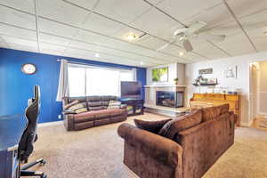 Living room with a drop ceiling, carpet, ceiling fan, a tiled fireplace, and an office area