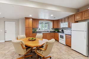 Kitchen with white appliances, dark countertops, recessed lighting, and brown cabinetry