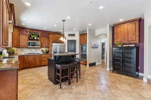 Kitchen featuring arched walkways, brown cabinetry, recessed lighting, a kitchen island, and a kitchen bar