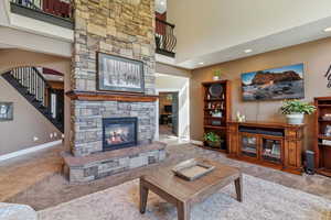 Carpeted living room with a fireplace, stairs, recessed lighting, and a high ceiling