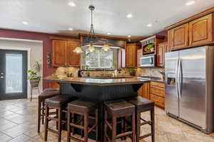 Kitchen with stainless steel appliances, backsplash, a breakfast bar area, brown cabinets, and recessed lighting