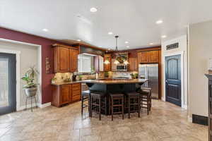 Kitchen with stainless steel appliances, brown cabinets, a breakfast bar, recessed lighting, and dark stone countertops