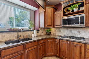 Kitchen with appliances with stainless steel finishes, dark stone counters, backsplash, and brown cabinets