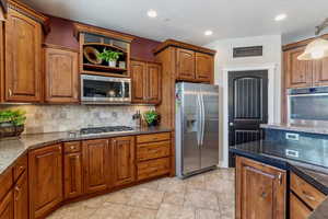 Kitchen with stainless steel appliances, decorative backsplash, dark stone counters, brown cabinets, and recessed lighting