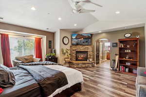 Bedroom featuring arched walkways, lofted ceiling, wood finished floors, a fireplace, and recessed lighting