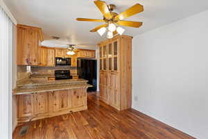Kitchen with a peninsula, black appliances, dark wood-style flooring, decorative backsplash, and ceiling fan