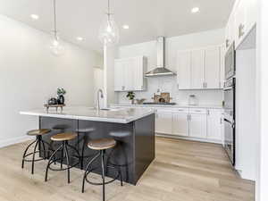 Kitchen with a kitchen breakfast bar, white cabinetry, pendant lighting, backsplash, and a center island with sink