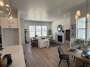 Living area with light wood-type flooring, a textured ceiling, a chandelier, a glass covered fireplace, and recessed lighting
