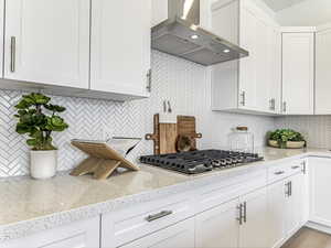 Kitchen featuring decorative backsplash, wall chimney exhaust hood, white cabinets, and light stone countertops