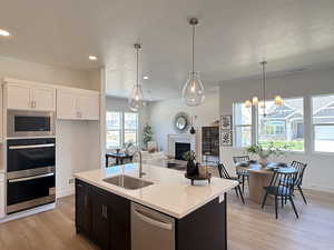 Kitchen featuring appliances with stainless steel finishes, a textured ceiling, a glass covered fireplace, white cabinets, and light wood-style flooring