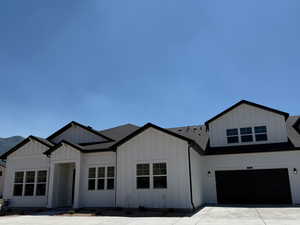 Modern farmhouse style home featuring board and batten siding, an attached garage, driveway, and roof with shingles