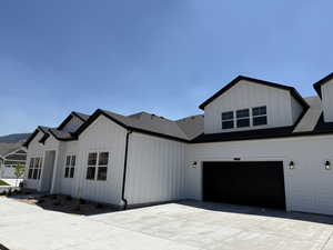 View of front of home with board and batten siding, concrete driveway, a shingled roof, and a garage
