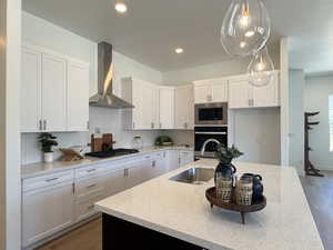 Kitchen with wood finished floors, appliances with stainless steel finishes, decorative backsplash, a textured ceiling, and wall chimney range hood