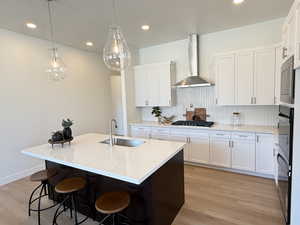 Kitchen with backsplash, light wood-style flooring, a breakfast bar, light stone countertops, and a center island with sink