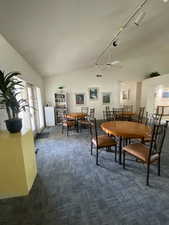 Dining space with lofted ceiling, rail lighting, dark colored carpet, and ceiling fan