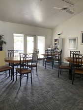 Dining space with lofted ceiling, healthy amount of natural light, ceiling fan, and dark colored carpet
