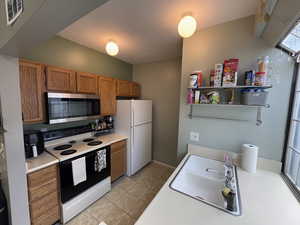 Kitchen with electric stove, stainless steel microwave, brown cabinets, light countertops, and freestanding refrigerator
