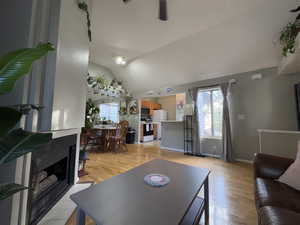 Living area featuring lofted ceiling, light wood-style floors, a fireplace with flush hearth, and a ceiling fan