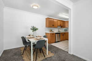 Kitchen featuring light carpet, decorative backsplash, crown molding, light countertops, and dishwasher