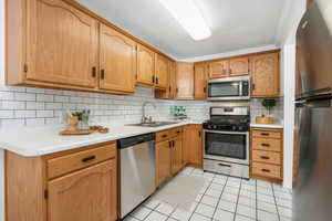 Kitchen with stainless steel appliances, light tile patterned flooring, tasteful backsplash, and light countertops