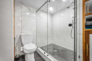 Downstairs Bathroom featuring a marble finish shower, tile patterned flooring, and tile walls.