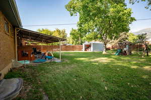 Fenced backyard with a playground and a storage unit.