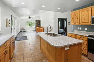 Kitchen featuring stove, vaulted ceiling, a center island with sink, ceiling fan, and recessed lighting