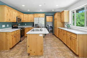 Kitchen featuring independent washer and dryer, appliances with stainless steel finishes, an island with sink, recessed lighting, and light stone countertops