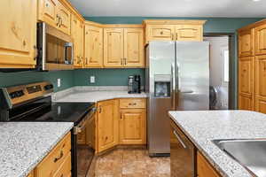 Kitchen featuring stainless steel appliances, light brown cabinets, and light stone countertops
