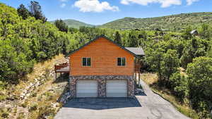 View of home's exterior with a forest view, an attached garage, asphalt driveway, and faux log siding