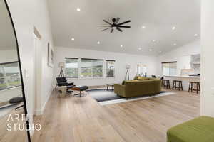 Living room with light wood flooring, high vaulted ceiling, windows overlooking backyard, recessed lighting, and ceiling fan