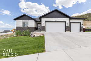 View of front facade with an attached garage, stone siding, board and batten siding, a front lawn, and concrete driveway