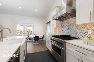 Kitchen featuring Viking range, vaulted ceiling, wall chimney exhaust hood, french doors, and white cabinets