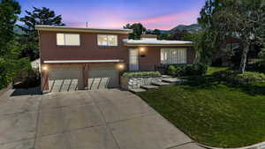 Split level home with brick siding, a front lawn, driveway, an attached garage, and a chimney