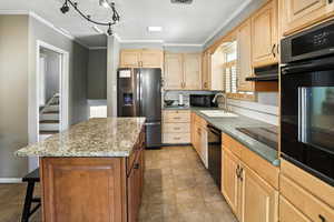 Kitchen with light brown cabinetry, black appliances, crown molding, a center island, and a breakfast bar