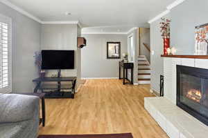 Living room featuring ornamental molding, wood finished floors, a brick fireplace, and stairway